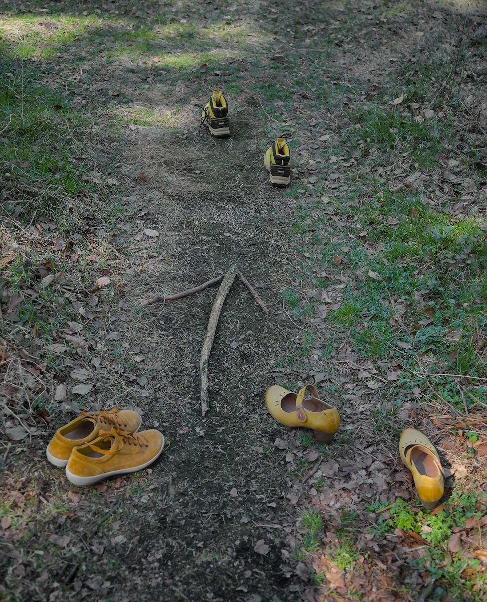 Drei gelbe Schuhe folgen einem Pfeil aus Stöcken auf einem Waldweg
